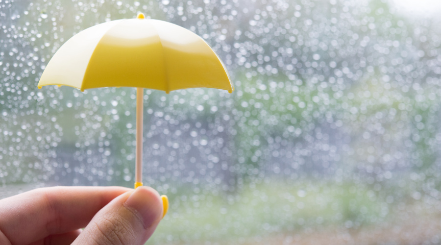 雨が降る窓際で黄色の傘のおもちゃを持つ手